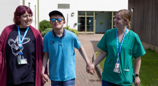 Female nurse and staff member walking and holding hands with male student