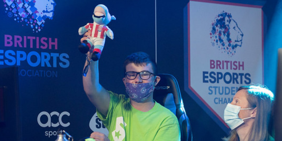 Male student holding up Stoke City FC toy mascot after scoring a goal in eSports tournament