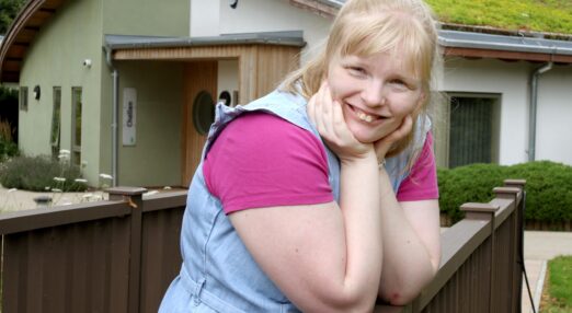 Tallulah smiling and standing against a wooden bannister