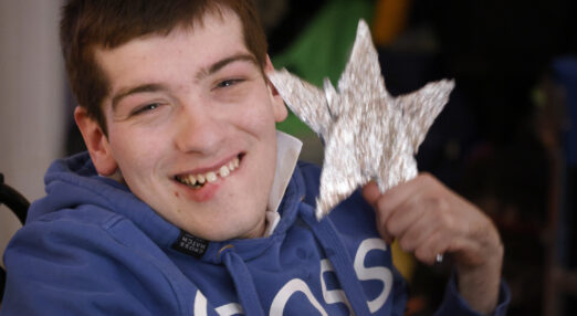 Man wearing a blue hoodie with white writing holding up a silver star