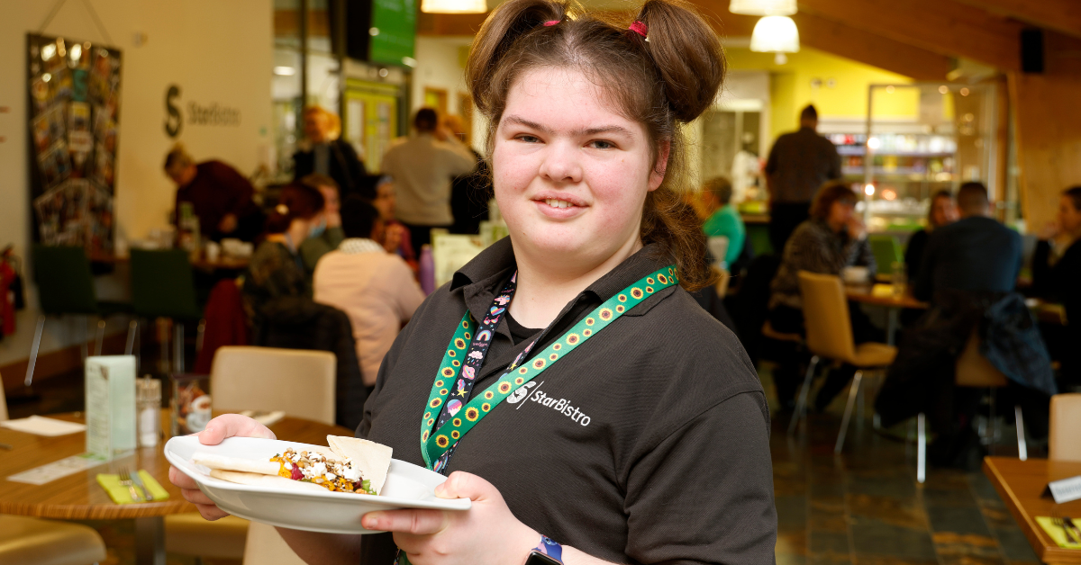 Sophie smiling holding up a plate of food in StarBistro