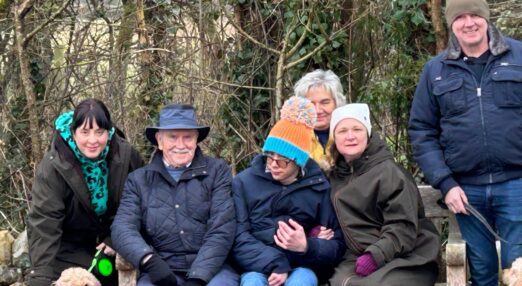 Elliott and his family sitting on a bench with a dog outside.