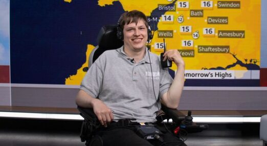 Joe smiling in front of weather screen at BBC studio